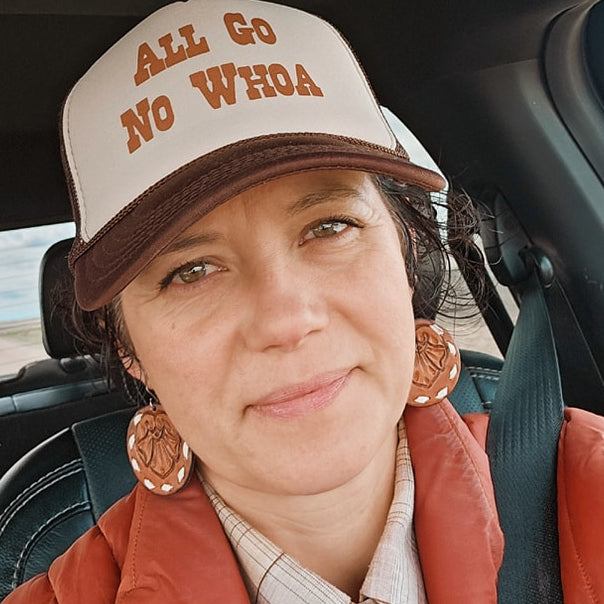 Person wearing a cap with 'All Go No Whoa' text inside a car.