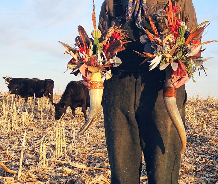 Person holding western decor horn flower arrangements in a field with cows.