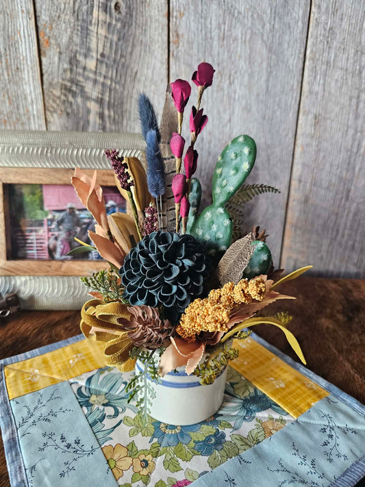 Decorative floral arrangement with cacti on a tablecloth in front of a wooden wall.