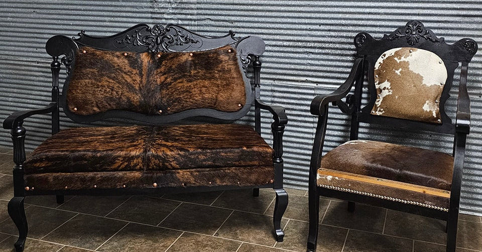 Vintage-style sofa and chair with cowhide upholstery against a wooden paneled wall.