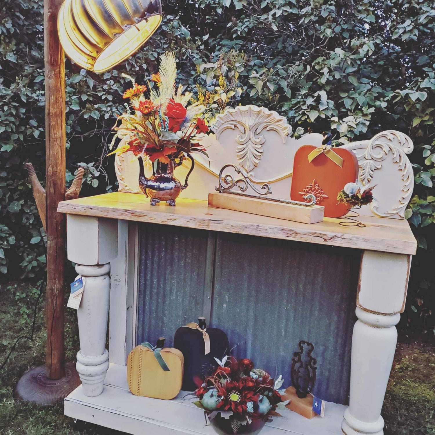 Decorative outdoor setup with a white mantelpiece, pumpkins, and floral arrangements against a natural background.