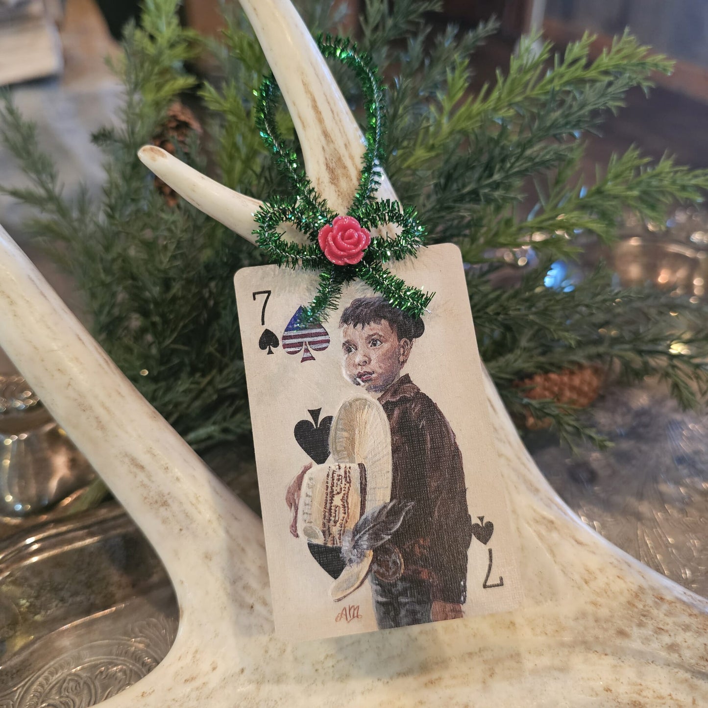 Vintage style boy holding a cowboy hat playing card Christmas ornament hanging on an antler