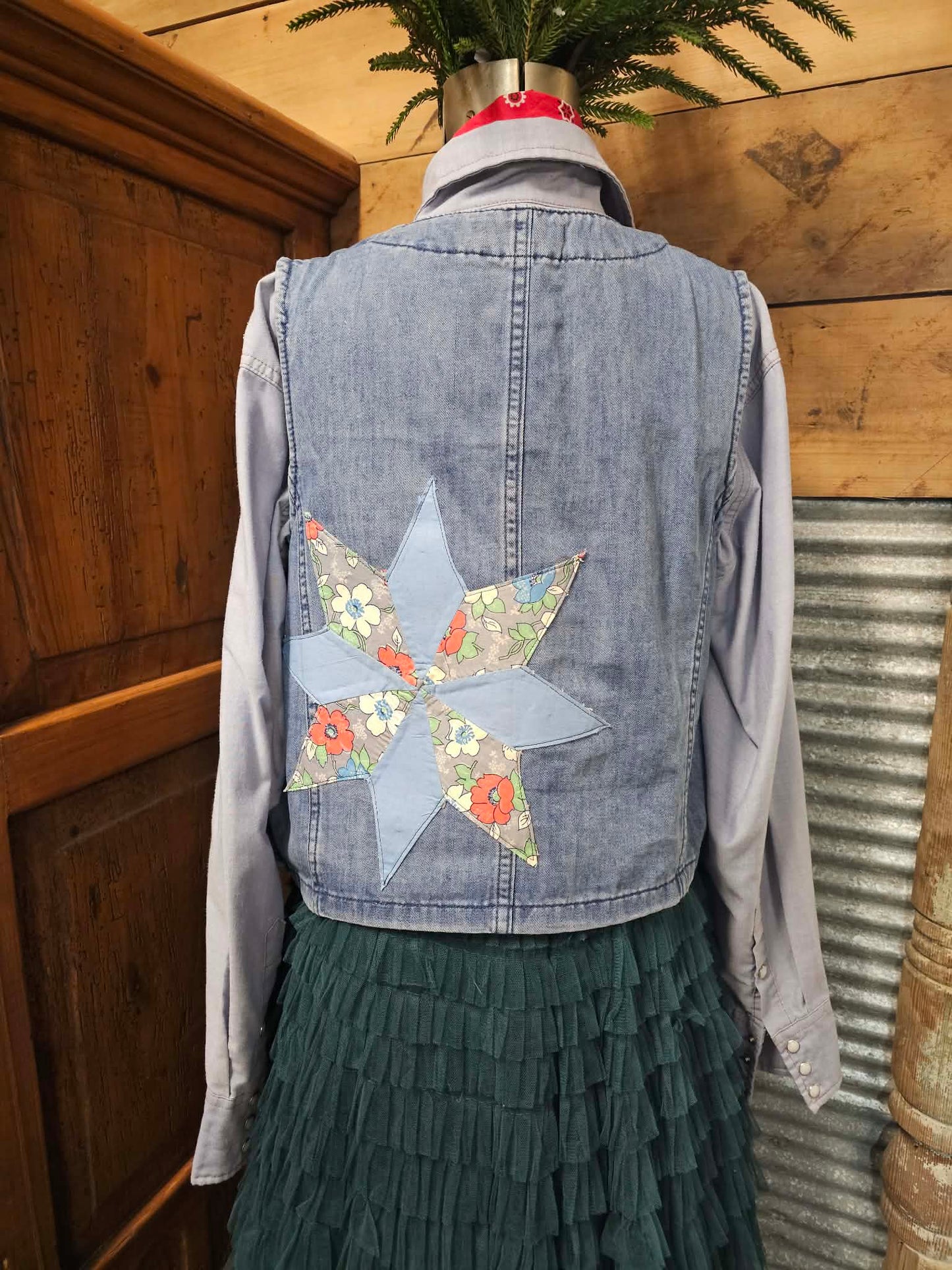 Denim vest with a floral star quilted on the back against a wooden wall.