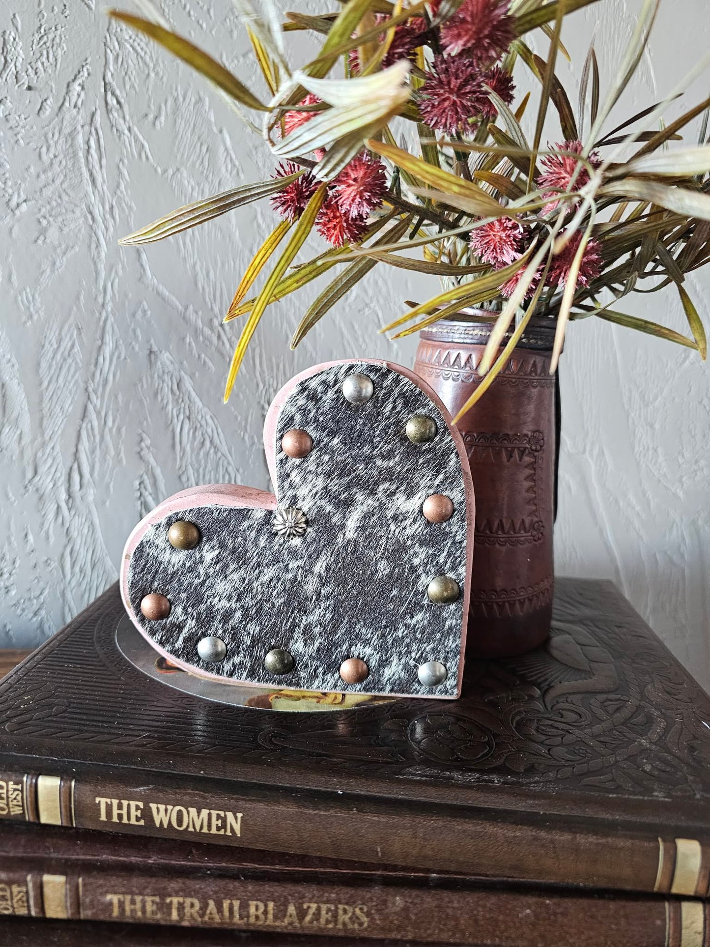 Decorative heart-shaped light on a stack of books with a vase of flowers in the background.