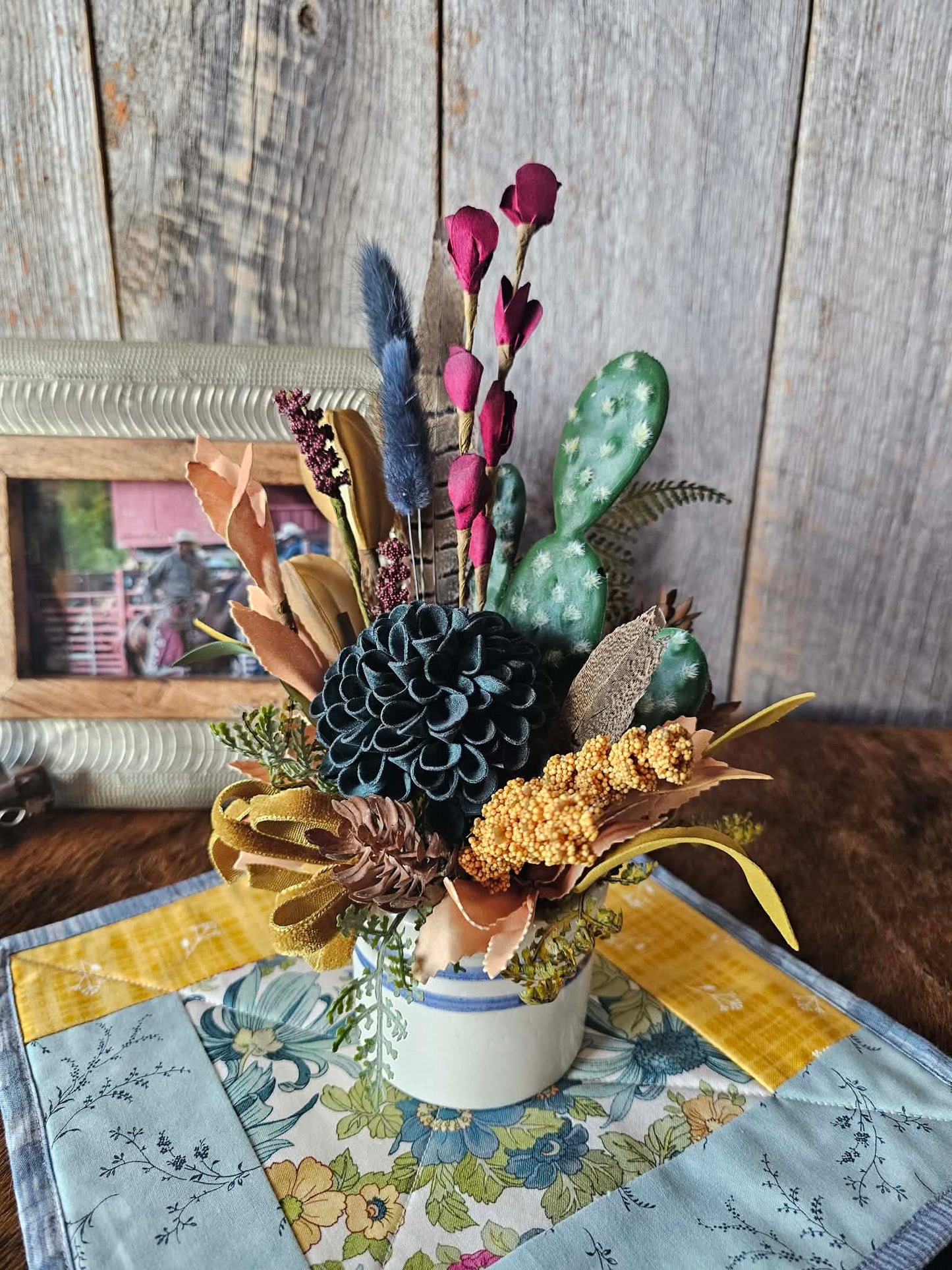 Decorative floral arrangement with cacti on a tablecloth in front of a wooden wall.