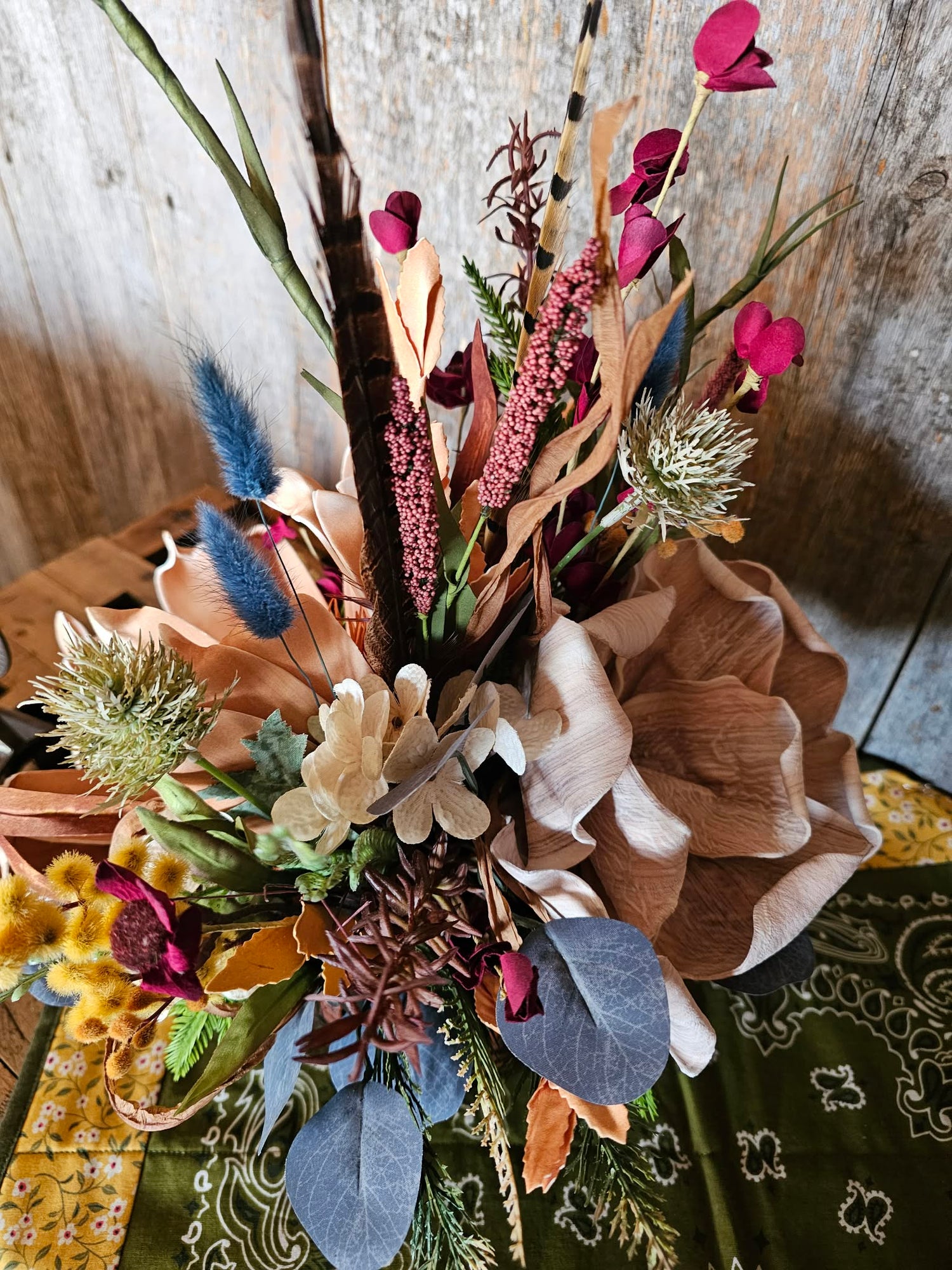 Bouquet of flowers with brown, green, and purple tones on a patterned fabric background.