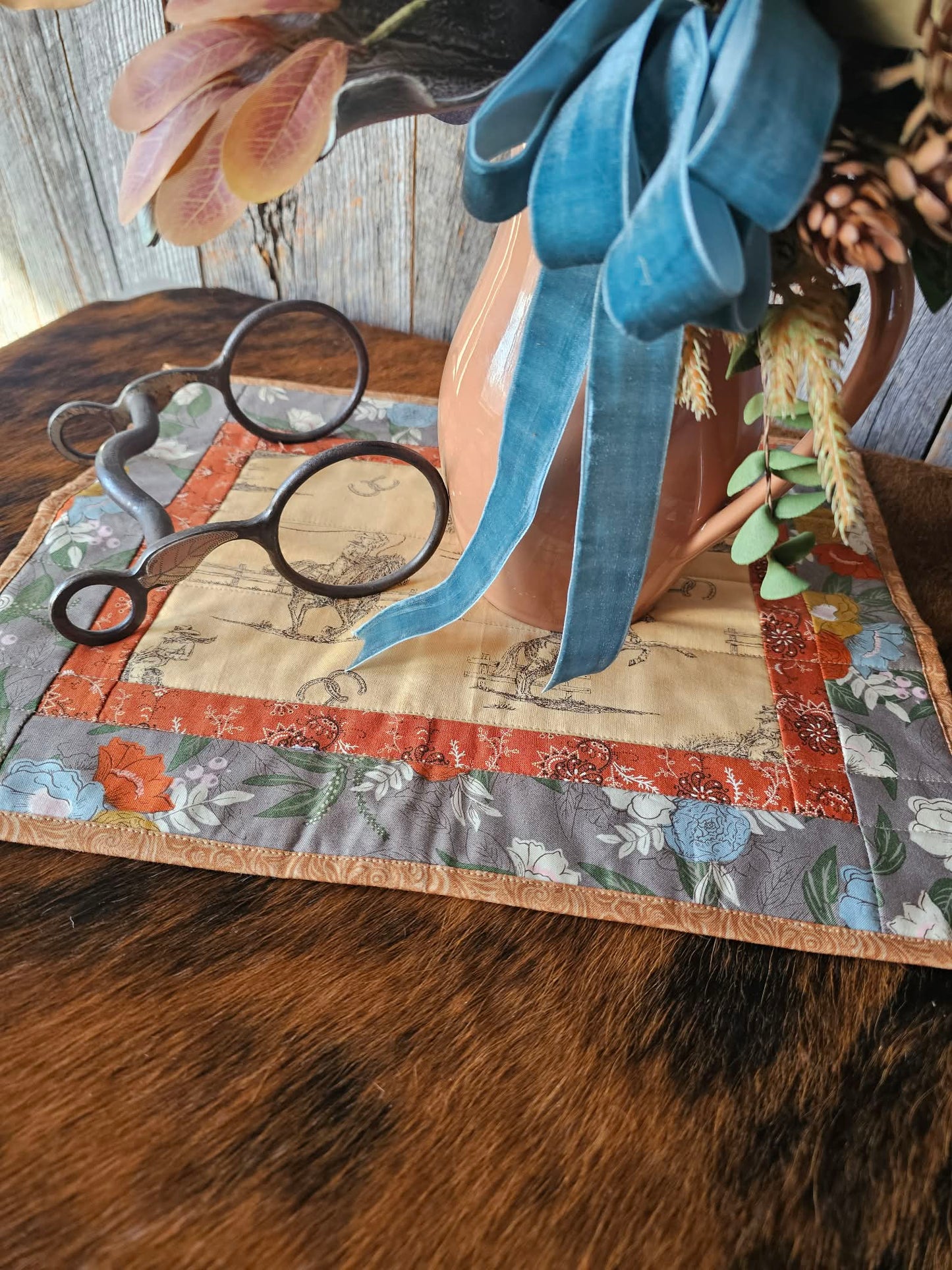 Decorative table setting with floral arrangement, bit, and fabric on a wooden surface.