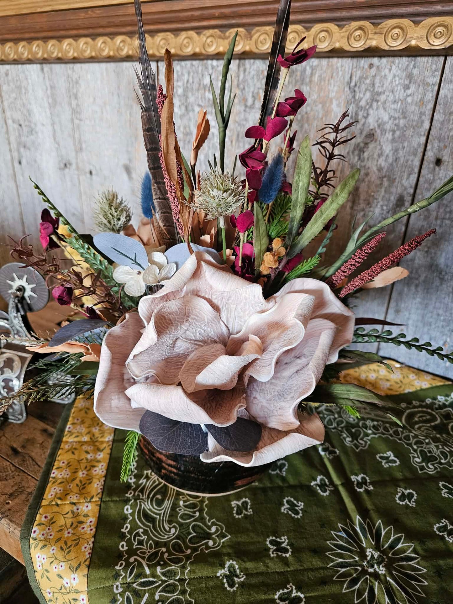 Floral arrangement with a large beige flower on a patterned tablecloth.